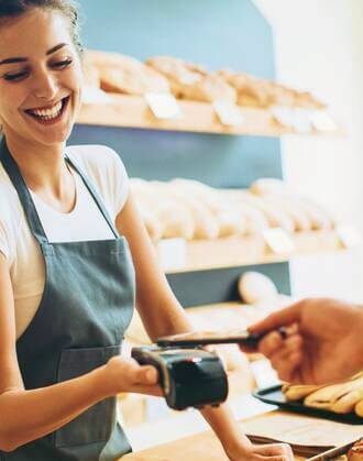 Atendente sorrindo enquanto cliente paga utilizando maquininha